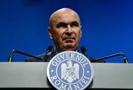 Premierul interimar Ilie Bolojan vorbind de la tribuna oficială a Guvernului României, având în față sigla oficială a Executivului