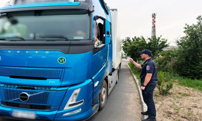 Polițist de frontieră efectuând un control asupra unui camion albastru în cadrul unei acțiuni privind o tentativă de contrabandă cu insecticid
