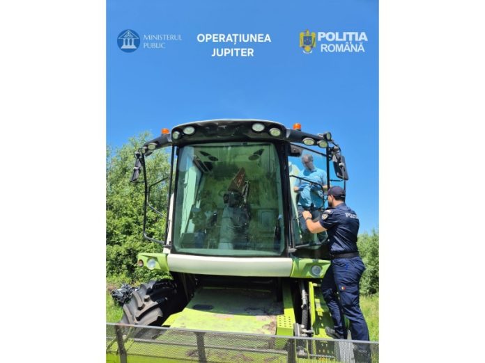 Un ofițer de poliție român în uniformă urcă scările unei mari combine agricole verzi și albe, verificând-o pe un câmp în plină zi însorită. Logo-uri suprapuse: Ministerul Public, Operațiunea JUPITER, Poliția Română.