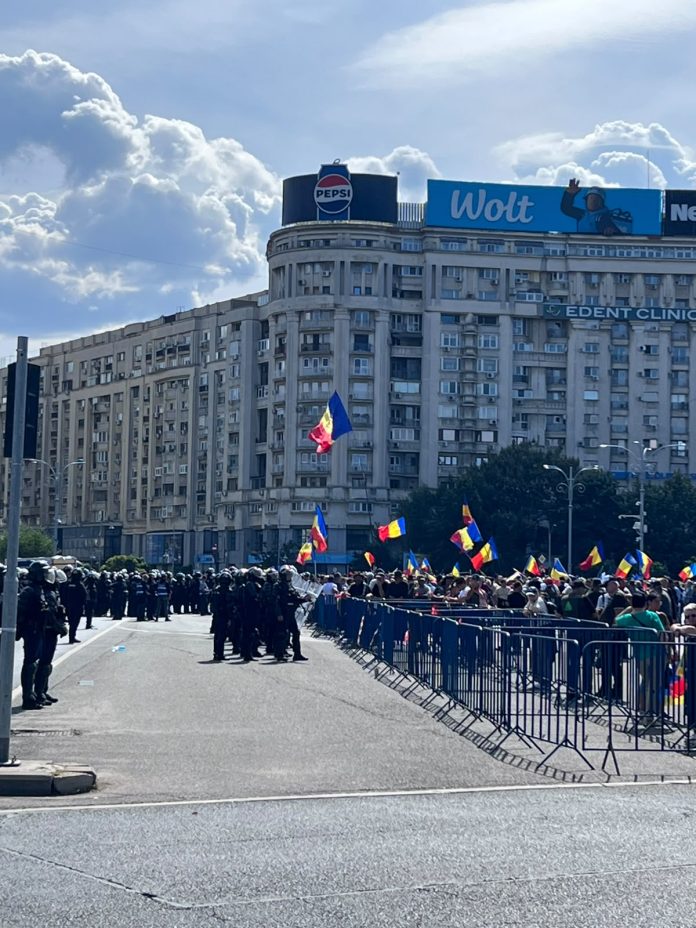 Cordon de jandarmi în echipament de intervenție și protestatari cu steaguri tricolore la protestul oierilor din Piața Victoriei, București, în fața Guvernului